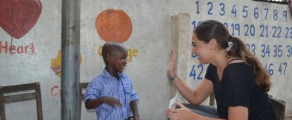 A child at a daycare centre in Ghana goes in for a high five with a volunteer during class. A Childcare volunteer in Ghana offers a child a high five for successfully completing an educational task.